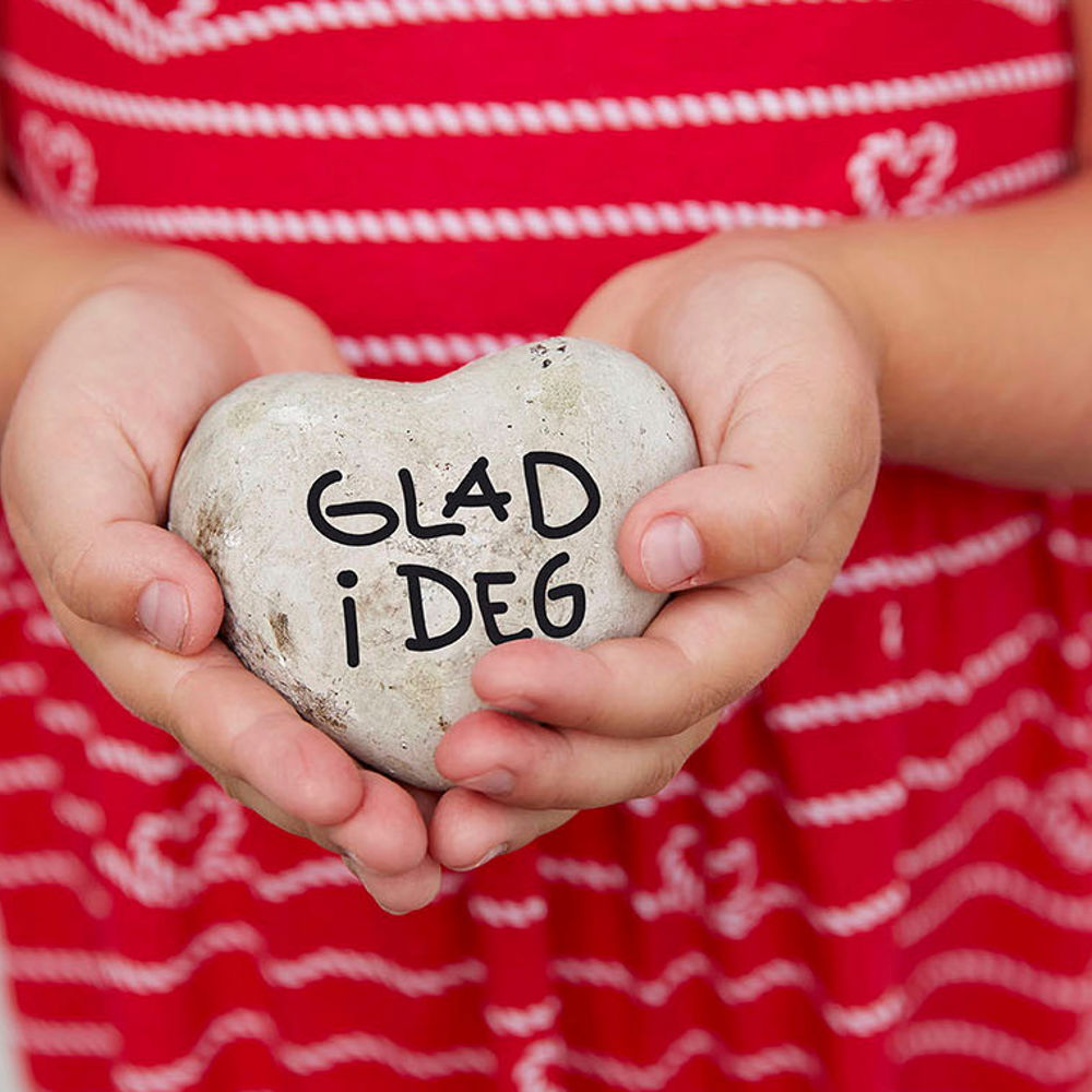 Children hold stones shaped like hearts with "love you" written on them. Photo.