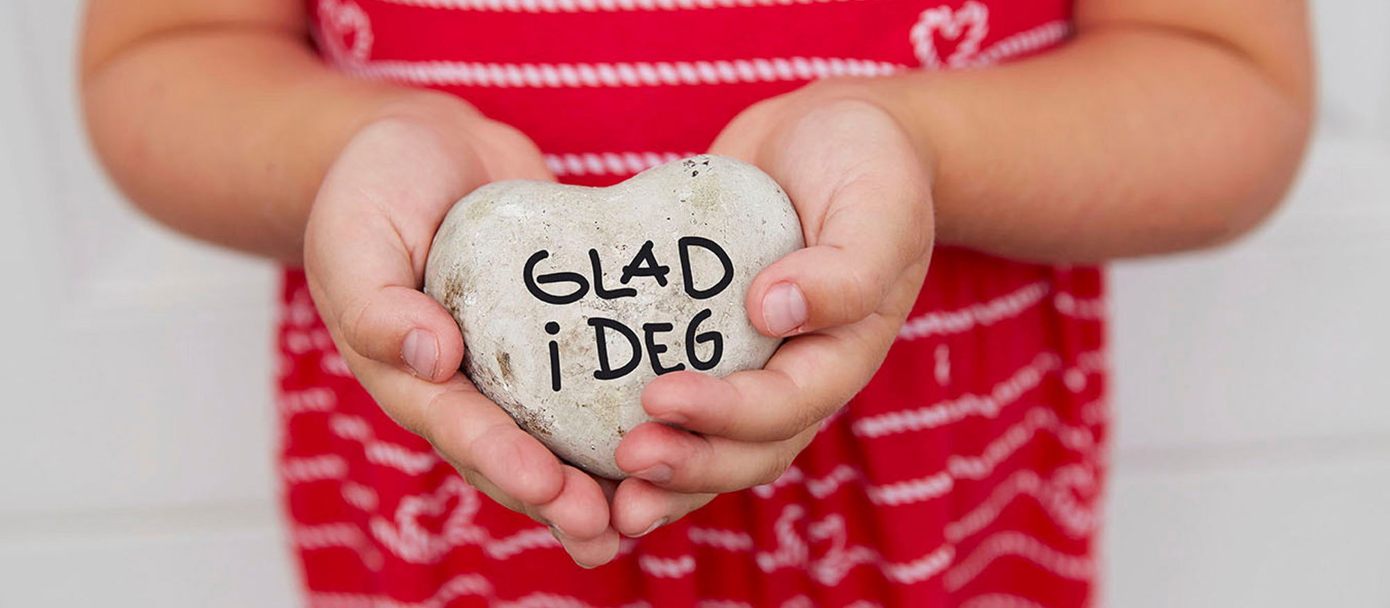 Children hold stones shaped like hearts with "love you" written on them. Photo.