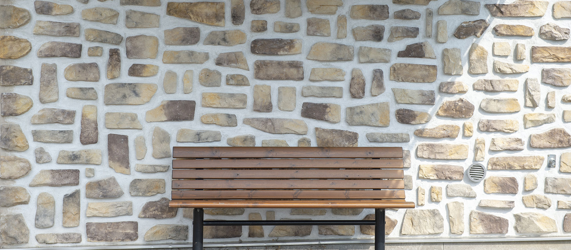 Bench standing in front of a brick wall. Photo. 