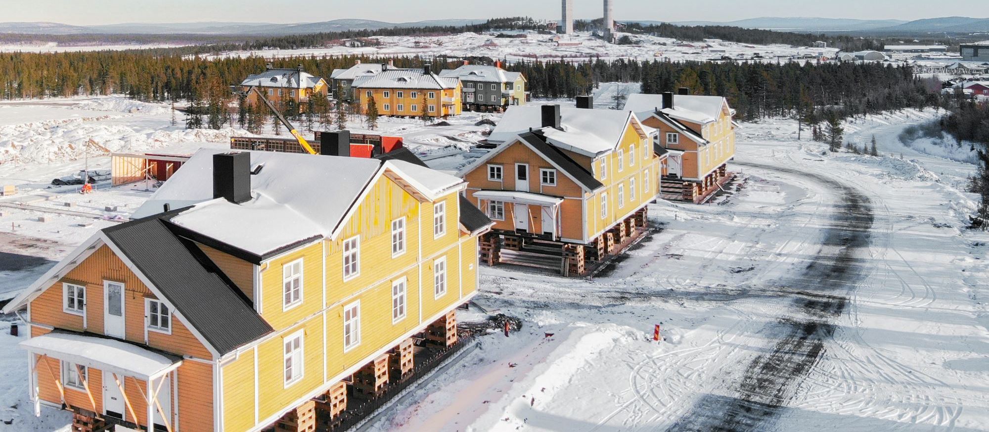 Vi flyttar “Gula raden” i Kiruna. Tre stora gula trähus har lyfts upp på pallar ovanför marken i snöig omgivning. 